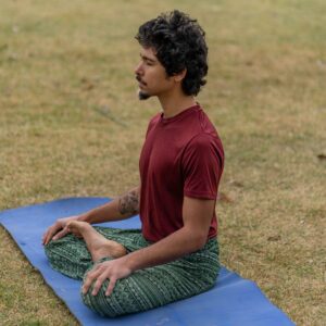 A man meditating in a relaxed posture on a blue yoga mat in a grassy field.